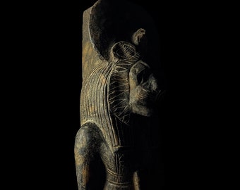 May include: A dark gray stone sculpture of a lion-headed deity with a headdress. The sculpture is carved in detail and has a weathered appearance.