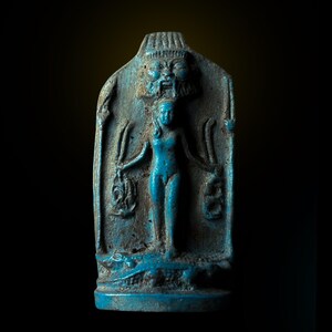 May include: A blue glazed ceramic stele depicting an Egyptian goddess with a crocodile at the base. The goddess is standing with her arms outstretched, holding a symbol in each hand. Above her head is a depiction of a god's face.