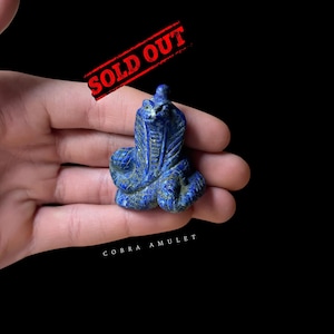 Op de afbeelding: Een klein, blauw lapis lazuli cobra amulet. Het amulet is gegraveerd in de vorm van een cobra met zijn kop omhoog en zijn mond open. Het amulet is een traditioneel Egyptisch symbool van bescherming.