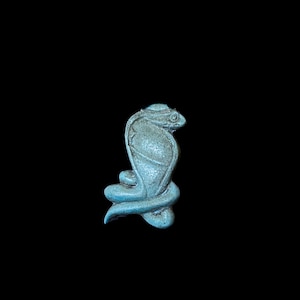 Könnte beinhalten: Türkisfarbene Kobra-Figur, aufgerollt und aufrecht, vor schwarzem Hintergrund. Der Kopf der Schlange ist erhoben, mit detaillierten Schuppen und einer Kapuze. Die Skulptur scheint aus einem steinartigen Material zu bestehen.