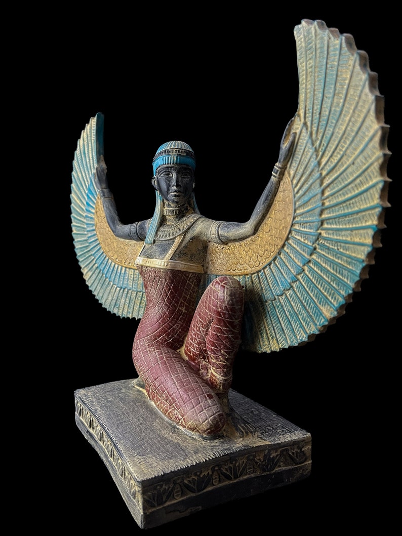 Puede incluir: Una estatua alada de una diosa egipcia con los brazos extendidos, arrodillada sobre una base. La estatua est&aacute; pintada en tonos dorados, azules, rojos y negros.