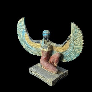 Puede incluir: Una estatua alada azul y dorada de una diosa egipcia con un tocado azul. La diosa est&aacute; arrodillada sobre una base negra con tallas intrincadas.