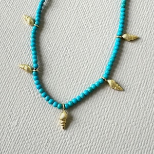 Turquoise necklace embellished with five gold plated sea shell pendants and gold plated lobster claw closure