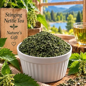 May include: A white ceramic bowl filled with dried green stinging nettle leaves. Next to the bowl is a wooden sign with the text Stinging Nettle Tea Nature's Gift and a heart symbol. Fresh green nettle plants and a glass of tea are visible.