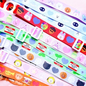 May include: A collection of colorful lanyards with various patterns and designs. The lanyards feature repeating images of hearts, smiley faces, and other cute illustrations. Some lanyards have the text "INSIDE NAMJOON'S BRAIN". Each lanyard has a white plastic buckle.