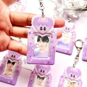 Pode incluir: Chaveiro de foto roxo e branco com design de coelho. O chaveiro tem uma janela de plástico transparente para inserir uma foto. O chaveiro está pendurado em uma corrente prateada.