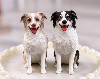 May include: Two dog figurines sitting on a white frosted cake. One figurine is a light brown and white dog, and the other is a black, white, and tan dog. Both figurines have open mouths with visible red tongues and detailed fur textures.