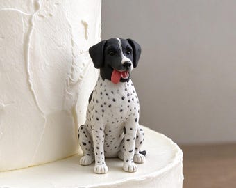 May include: A small, hand-sculpted figurine of a white dog with black spots and a black head, featuring a pink tongue sticking out, positioned on the tier of a white frosted cake with a textured, swirled buttercream finish.
