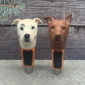 May include: Two ceramic dog head beer tap handles. The handle on the left is white with black spots and the handle on the right is brown. Both handles have a black chalkboard sign.