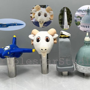 May include: Four different beer tap handles. The first is a blue and yellow airplane, the second is a white ram head, the third is a gray block with the word "Heydon" on it, and the fourth is a green dome with a white top.