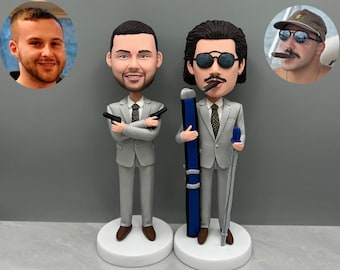 May include: Two custom bobbleheads, one holding a pair of guns and the other holding a ski pole and a walking stick. Both bobbleheads are wearing gray suits and have realistic facial features.