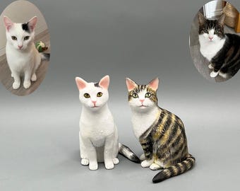 May include: Three realistic cat figurines. One white cat with black markings is sitting with its tail curled around its legs. One tabby cat with brown and white stripes is sitting with its tail curled around its legs. One black and white cat is sitting with its tail curled around its legs.