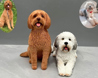May include: Two custom-made dog figurines, one brown and one white with gray markings. The brown figurine is sitting upright, while the white figurine is lying down. Both figurines have realistic features and are made of clay.