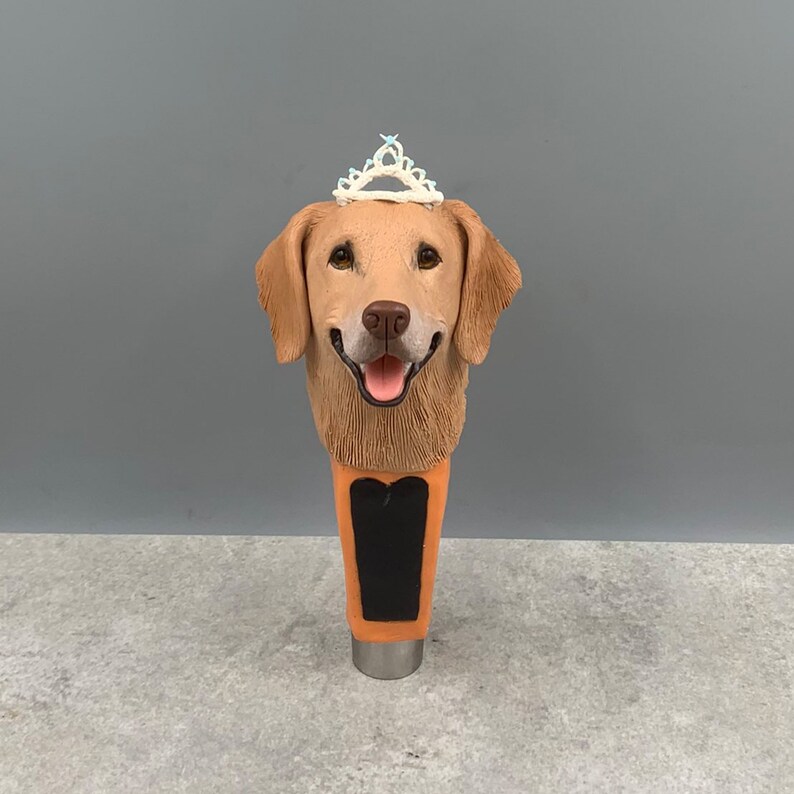 Może przedstawiać: Głowa golden retrievera z białą tiarą na g&oacute;rze, przymocowana do brązowej i pomarańczowej wylewki do piwa.