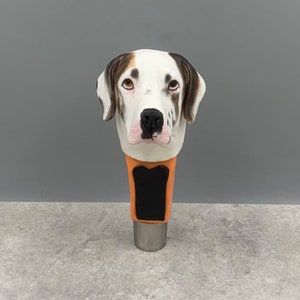 May include: A white, black, and brown ceramic beer tap handle with a dog's head. The dog has brown eyes and a black nose.