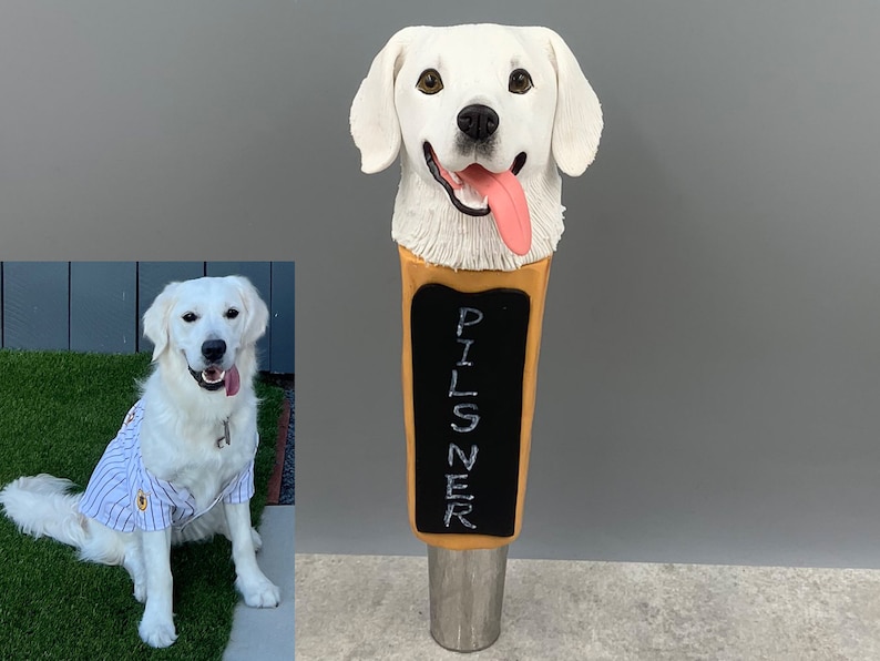 May include: A white ceramic dog head sculpture with a tongue sticking out, mounted on a wooden beer tap handle. The handle is labeled "PILSNER".