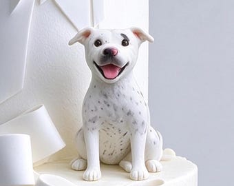 May include: A white dog figurine with black spots, a pink nose, and an open mouth showing a pink tongue. The dog is sitting upright and is positioned on top of a white cake decorated with large, sculpted white fondant ribbons and bows.