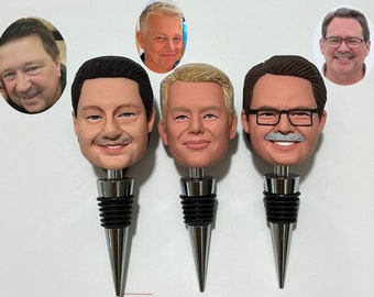 May include: Three personalized wine bottle stoppers with different faces. Each stopper is made of a silver metal with a black rubber base.