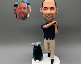 May include: A personalized golf-themed figurine of a man in a navy blue polo shirt and khaki pants, poised to swing a golf club. A golf bag and ball are next to him. A photo is in the background.