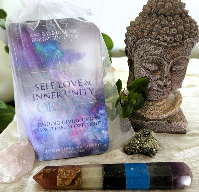 May include: A 62-card deck and digital guidebook titled "Self Love & Inner Unity Oracle: Finding Divine Union as Within, So Without." Illustrated and written by Senna Zen. The deck is in a white organza bag with a pink crystal, a small piece of pyrite, and a multi-colored crystal wand.