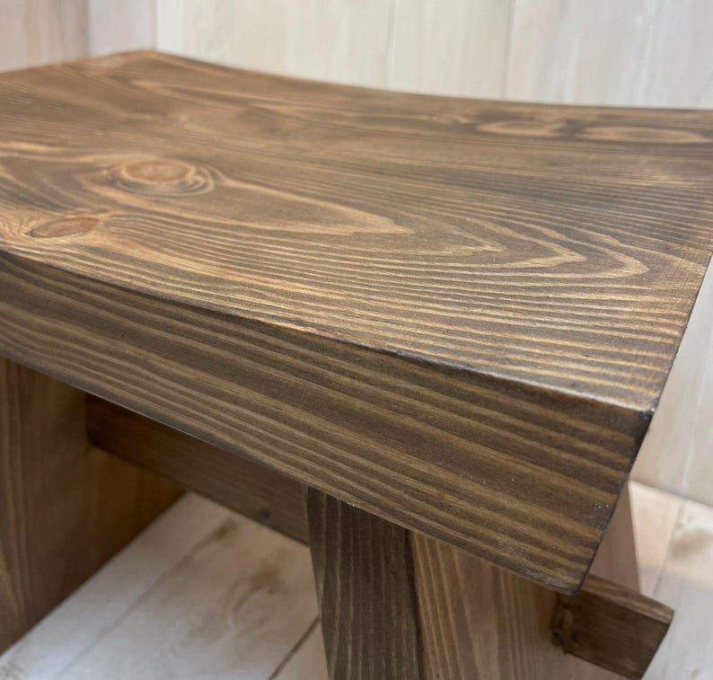 K&ouml;nnte beinhalten: Ein dunkler brauner Holzhocker mit einer abgerundeten Oberseite und einem einfachen, robusten Design.