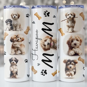 May include: A white tumbler adorned with images of Havanese puppies, paw prints, and bone shapes. The design includes the name "HavaPoo" and the letter "M". The tumbler has a silver lid and is likely made of stainless steel, suitable for hot or cold drinks.