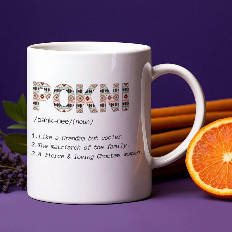 May include: White ceramic mug with the word "POKNI" in a patterned design. The mug includes the definition of "POKNI" as "Like a Grandma but cooler," "The matriarch of the family," and "A fierce & loving Choctaw woman."