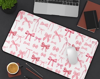 May include: A white desk mat with a pink watercolor bow pattern. The mat is designed for use with a computer mouse and keyboard.