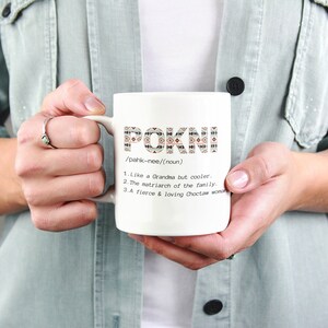 May include: White ceramic mug with the word "POKNI" in a patterned design. The mug includes a definition: "Like a Grandma but cooler," "The matriarch of the family," and "A fierce & loving Choctaw woman."