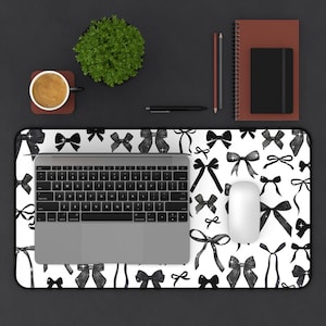 May include: A white desk mat with a black and white watercolor bow pattern. A laptop computer, a wireless mouse, and a cup of coffee are on the desk mat.