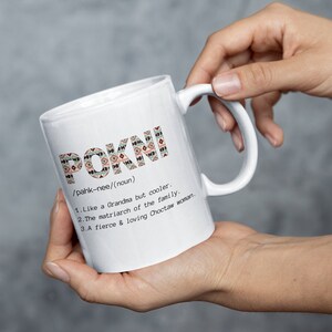 May include: White ceramic mug with the word "POKNI" in a patterned design. The mug includes a definition: "Like a Grandma but cooler. The matriarch of the family. A fierce & loving Choctaw woman."