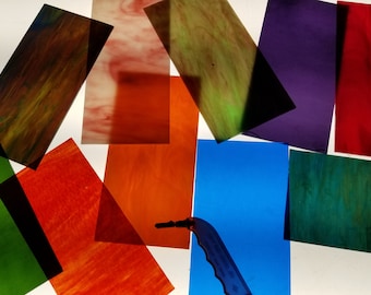 May include: Assortment of colorful glass sheets in various shades of green, blue, red, orange, and brown. The glass sheets are arranged in a random pattern on a white surface.