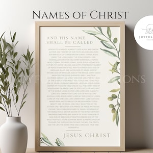 May include: Framed print titled "Names of Christ" with text listing various names. The print has a light wood frame and is decorated with watercolor-style green leaves. A white vase with green branches is in the foreground.