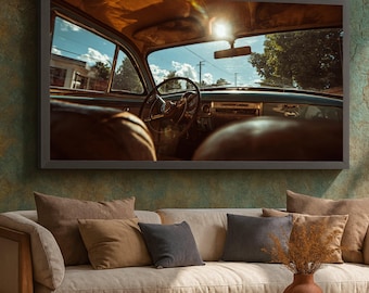 May include: A framed print depicting the interior of a classic car, seen from within. The steering wheel, dashboard, and front seats are in view. Sunlight streams through the windscreen, lighting the interior. The print hangs above a beige sofa with several cushions.