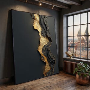 Op de afbeelding: Grote abstracte wandkunst met een donkergrijze achtergrond en een textuurontwerp in goud en zwart. Het kunstwerk is ingelijst in een zwarte lijst en leunt tegen een muur in een kamer met een raam met uitzicht op een stad.