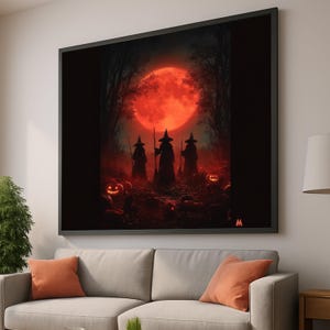 May include: A framed Halloween-themed artwork featuring three witch silhouettes in a dark forest under a large, red full moon. Carved jack-o'-lanterns are scattered in the foreground. The artwork is displayed above a gray sofa with orange throw pillows.