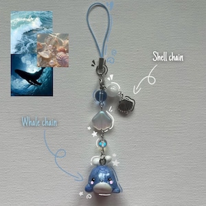 Op de afbeelding: Een telefoonhanger met een blauwe walvisbedel, een witte schelpbedel en doorschijnende blauwe en witte kralen aan een zilveren ketting met een lichtblauwe lus. De tekst "Whale chain" en "Shell chain" staat bij de betreffende bedels.