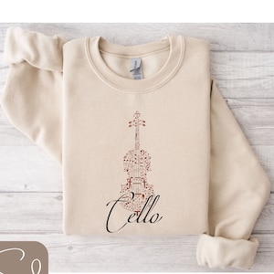 May include: A beige sweatshirt with a brown cello design made of musical notes. The word "Cello" is written in black cursive below the cello.