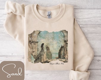 Puede incluir: Una sudadera beige con un estampado desgastado de estilo vintage de una mujer con un vestido blanco fluido de pie frente a un arco de piedra en ruinas. La impresión incluye una cita del poema "Annabel Lee" de Edgar Allan Poe: "Fue hace muchos, muchos años, en un reino junto al mar, que vivía una doncella que quizás conozcas por el nombre de Annabel Lee."