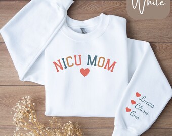 May include: White sweatshirt with the text "NICU MOM" in colourful letters with a red heart. The sleeve has three red hearts with the names "Lucas", "Clara", and "Gus" written below.