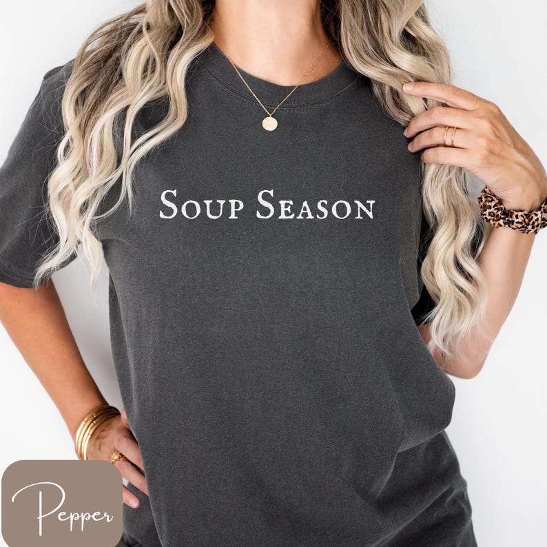 Puede incluir: Camiseta gris oscuro con la frase "Soup Season" en blanco. La camiseta tiene mangas cortas y un corte holgado. La palabra "Pepper" est&aacute; en un cuadrado marr&oacute;n claro en la esquina inferior izquierda.