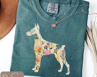 Può includere: T-shirt Comfort Colors verde acqua con una silhouette floreale di cane. Il cane è pieno di fiori colorati. Una collana d'oro con un ciondolo è drappeggiata sulla maglietta. La maglietta ha una piccola etichetta con la scritta "Comfort Colors".