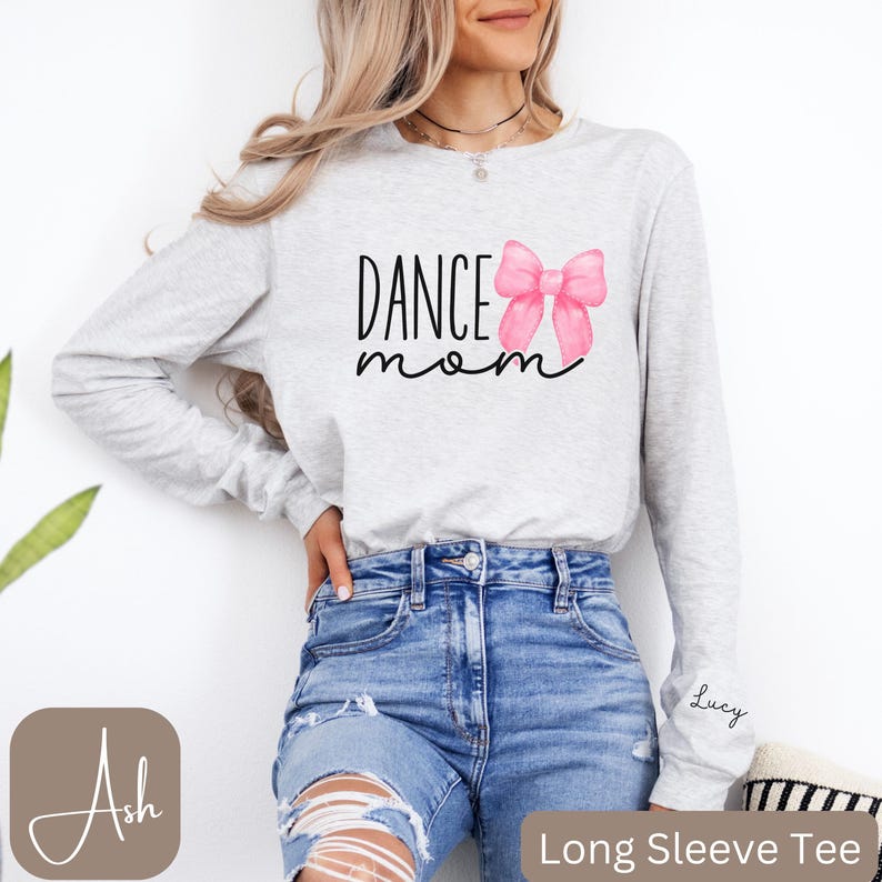 Może przedstawiać: Szara koszula z długim rękawem z napisem "Dance Mom" i r&oacute;żową akwarelową kokardką. Koszula ma napis "Lucy" na rękawie.