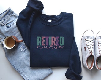May include: A navy blue sweatshirt with the text "RETIRED nurse" in colorful, distressed lettering. The sweatshirt is paired with blue jeans and white sneakers.