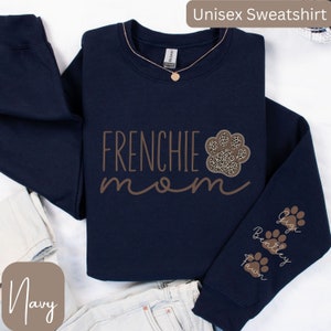 May include: Navy blue unisex sweatshirt with the text "Frenchie mom" in brown lettering. A paw print with a leopard print design is next to the text. The sleeve has three paw prints with the names Gigi, Bentley, and Fawn.