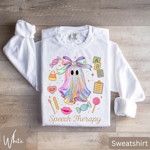 May include: White sweatshirt with a colorful ghost graphic, candies, and the words "Speech Therapy." The ghost is adorned with a bow and sparkles. The design includes ABC blocks, a clipboard, and a lollipop.