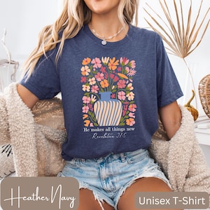 May include: A heather navy blue unisex t-shirt with a floral design and the text "He makes all things new Revelation 21:5".