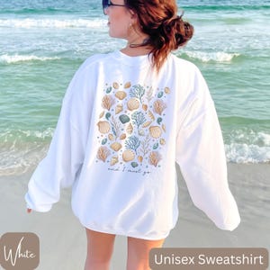 K&ouml;nnte beinhalten: Wei&szlig;er Unisex-Sweatshirt mit einem Muschel- und Algenmuster auf der R&uuml;ckseite. Der Text "and I must go" ist unter dem Design gedruckt.