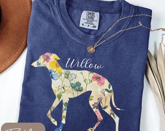 以下が含まれることがあります： フローラルの犬のシルエットと白いスクリプトで「Willow」という名前が入ったトゥルーネイビーのTシャツ。犬のデザインはカラフルな花が特徴です。ペンダント付きのゴールドネックレスがシャツにかけられています。