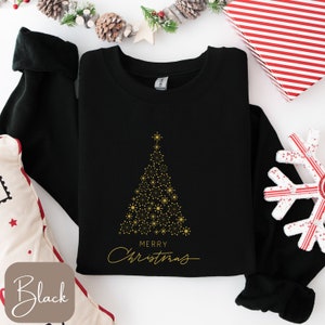 May include: Black sweatshirt with a gold Christmas tree design made of dots and snowflakes. The words "MERRY CHRISTMAS" are written in gold script below the tree. The word "Black" is in a brown box in the lower left corner.